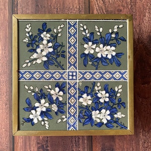 May include: A brass framed decorative tile with a green background and a blue and white floral pattern. The tile is divided into four sections, each with a different floral design.