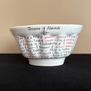 May include: White ceramic bowl with a recipe for "Mousse of Almonds" written in black and red script. The bowl is on a black surface. The recipe includes measurements like cups, ounces, and teaspoons.