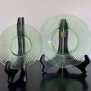 May include: Two green glass plates with a fluted design are displayed on black stands. The plates are clear and have a slight green tint.