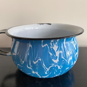 May include: A blue and white enamelware chamber pot with a black rim and handle.
