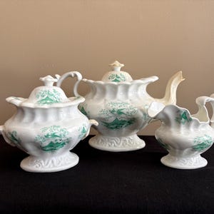 May include: A set of three ceramic mugs with a speckled, matte finish. Each mug features a different color: light blue, cream, and gray. The mugs have a simple, modern design and a comfortable handle.