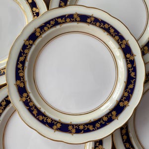 May include: Set of five white porcelain plates with a blue and gold floral design. The plates have a scalloped edge and are perfect for serving desserts or appetizers.