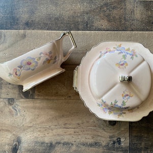 May include: A vintage pink and white floral patterned butter dish with a lid and a matching gravy boat. The dish has a gold trim and the lid has a small knob.