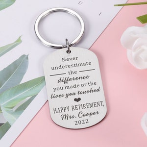 Pode incluir: Chaveiro de prata com uma etiqueta que diz "Nunca subestime a diferença que você fez ou as vidas que você tocou. Feliz aposentadoria, Sra. Cooper 2022".