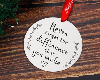 May include: White round bauble with a red ribbon and the text "Never forget the difference that you make" with a small heart at the bottom.