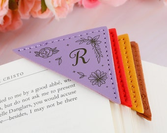 May include: A collection of colorful leather bookmarks in shades of purple, red, yellow, and brown. The purple bookmark features floral designs and the letter "R". The bookmarks are placed in an open book.
