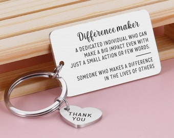Puede incluir: Llavero de plata con un dije en forma de corazón que dice "Gracias" y una etiqueta rectangular que dice "Difference maker Un individuo dedicado que puede tener un gran impacto incluso con una pequeña acción o pocas palabras. Alguien que marca la diferencia en la vida de los demás."