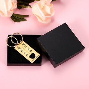 May include: Gold-tone keychain with two interlocking rings and two rectangular tags. The tags are engraved with the date "12.08.18" and the initials "B&G". The keychain is in a black gift box.