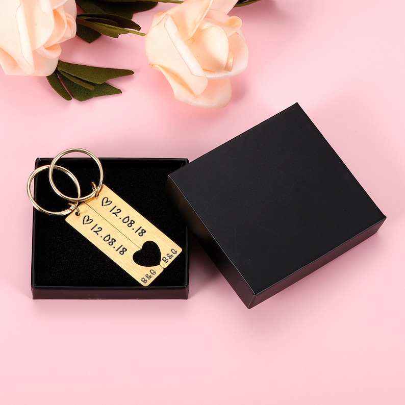May include: Gold-tone keychain with two interlocking rings and two rectangular tags. The tags are engraved with the date "12.08.18" and the initials "B&G". The keychain is in a black gift box.