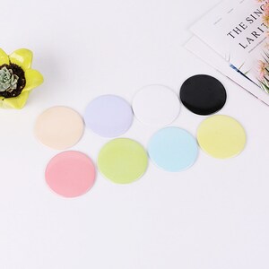 May include: Eight round, blank, colorful,  decorative,  paper or plastic,  circular,  stickers or badges.  The colors are light pink, light blue, light green, yellow, white, black, light peach, and lavender.
