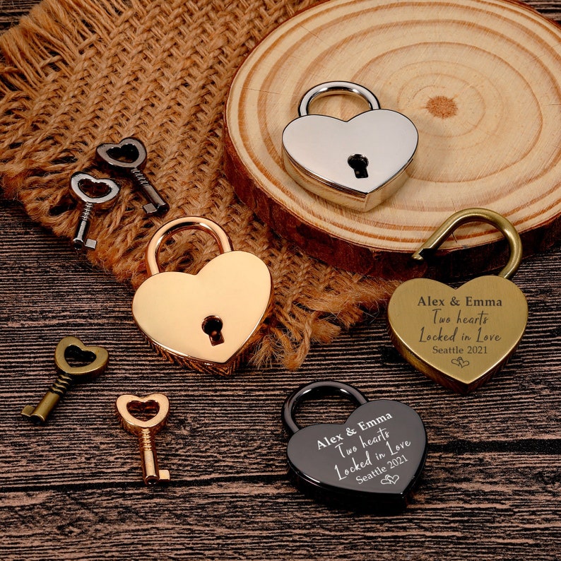 May include: Three heart-shaped padlocks with keys. One padlock is silver, one is gold, and one is black. The black and gold padlocks have the text "Alex & Emma Two hearts Locked in Love Seattle 2021" engraved on them.
