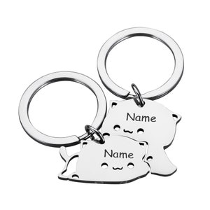 May include: Two silver keychains with cat-shaped charms. Each charm has the word "Name" engraved on it.