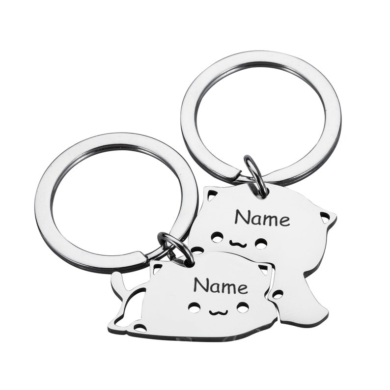 May include: Two silver keychains with cat-shaped charms. Each charm has the word "Name" engraved on it.
