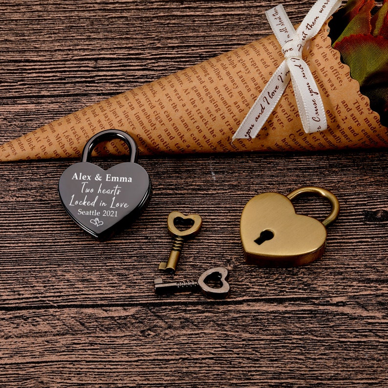 May include: A black heart-shaped padlock with the inscription "Alex & Emma Two hearts Locked in Love Seattle 2021" and a gold heart-shaped padlock with a keyhole. Two keys are also included, one with a heart-shaped head and one with a round head.