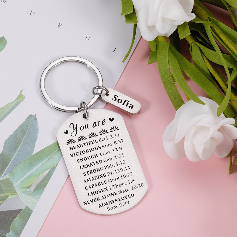 Puede incluir: Llavero de plata con una etiqueta en forma de coraz&oacute;n que dice "You are" seguida de una lista de afirmaciones positivas y vers&iacute;culos b&iacute;blicos. La etiqueta est&aacute; unida a un anillo de plata con una etiqueta m&aacute;s peque&ntilde;a que dice "Sofia".