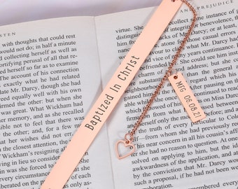 May include: A rose gold bookmark with a heart charm and a chain. The bookmark is engraved with the text "Baptized In Christ" and "MFG 06.08.21".