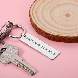 May include: Silver keyring with a rectangular tag that says "customized me here". The keyring is attached to a key and a split ring.