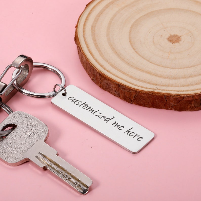May include: Silver keyring with a rectangular tag that says "customized me here". The keyring is attached to a key and a split ring.