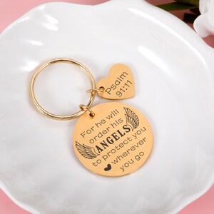 May include: Gold-toned keychain with a round charm that reads "For he will order his ANGELS to protect you wherever you go" and a heart-shaped charm that reads "Psalm 91:11".