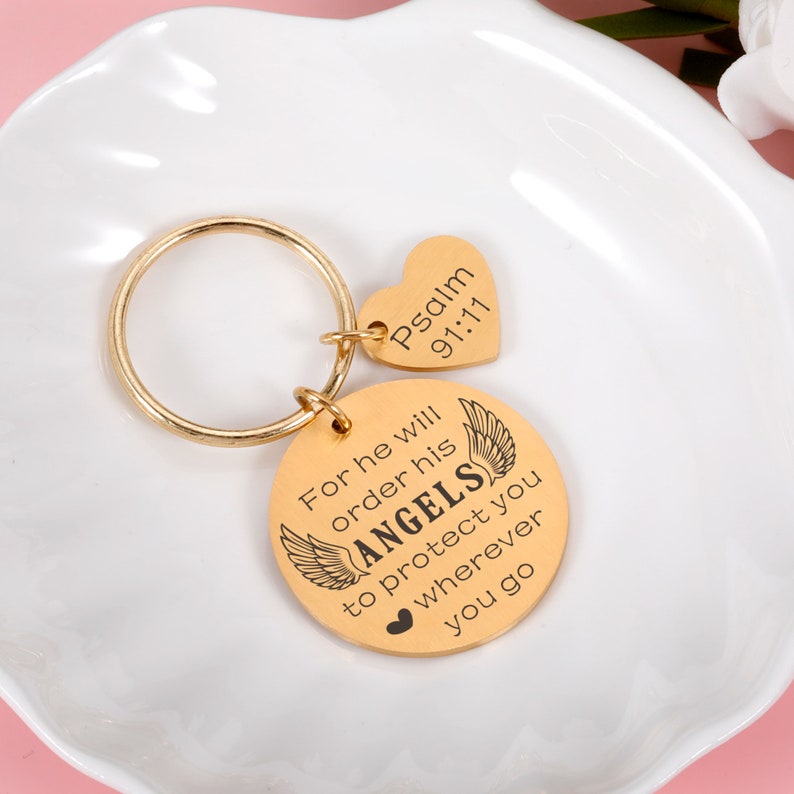 May include: Gold-toned keychain with a round charm that reads "For he will order his ANGELS to protect you wherever you go" and a heart-shaped charm that reads "Psalm 91:11".