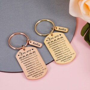 Puede incluir: Dos llaveros de tono dorado con dijes en forma de placa de identificaci&oacute;n. Los dijes tienen el texto "You are" seguido de una lista de afirmaciones positivas y vers&iacute;culos b&iacute;blicos. Los llaveros est&aacute;n personalizados con el nombre "Sofia" en cada etiqueta.