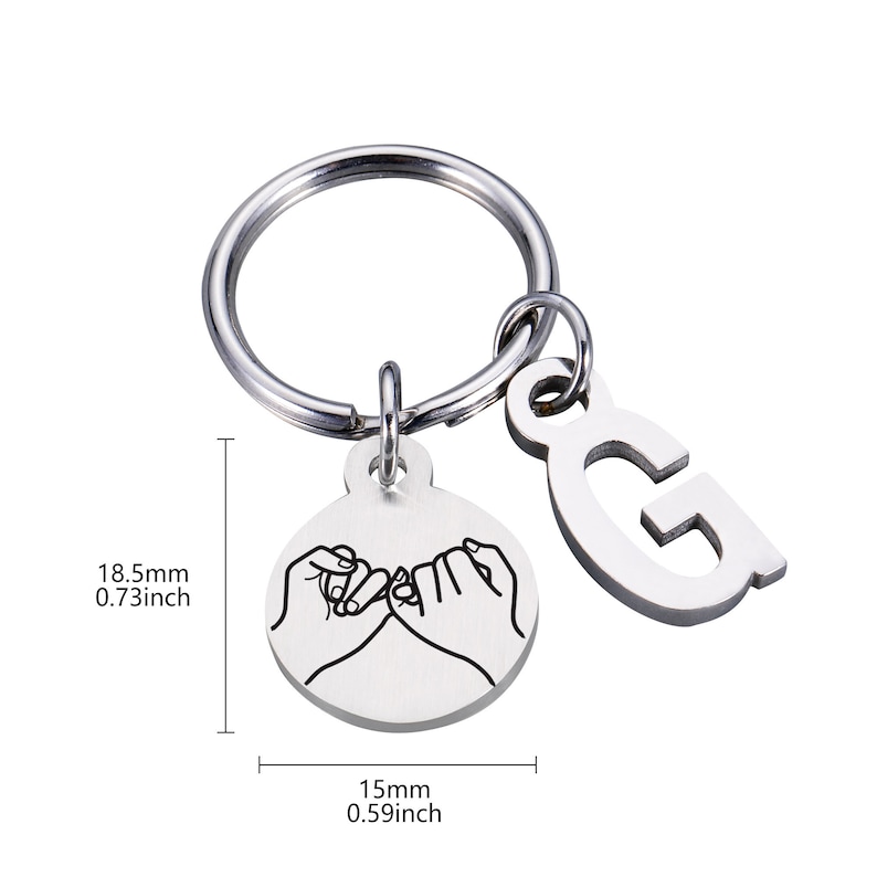 May include: Silver keychain with a circle charm featuring two hands making a pinky promise and a letter G charm. The keychain measures 0.73 inches in diameter and 0.59 inches in height.