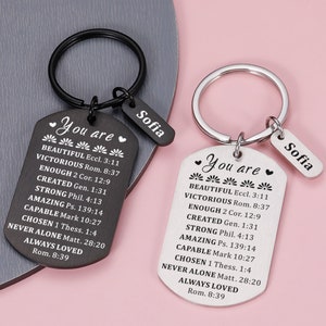 Puede incluir: Dos llaveros negros y plateados con una etiqueta que dice "You are" seguida de una lista de afirmaciones positivas y el nombre "Sofia" en una etiqueta m&aacute;s peque&ntilde;a.