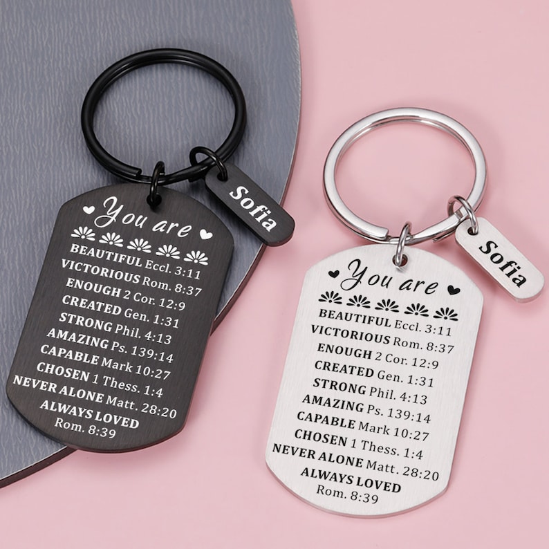 Puede incluir: Dos llaveros negros y plateados con una etiqueta que dice "You are" seguida de una lista de afirmaciones positivas y el nombre "Sofia" en una etiqueta m&aacute;s peque&ntilde;a.