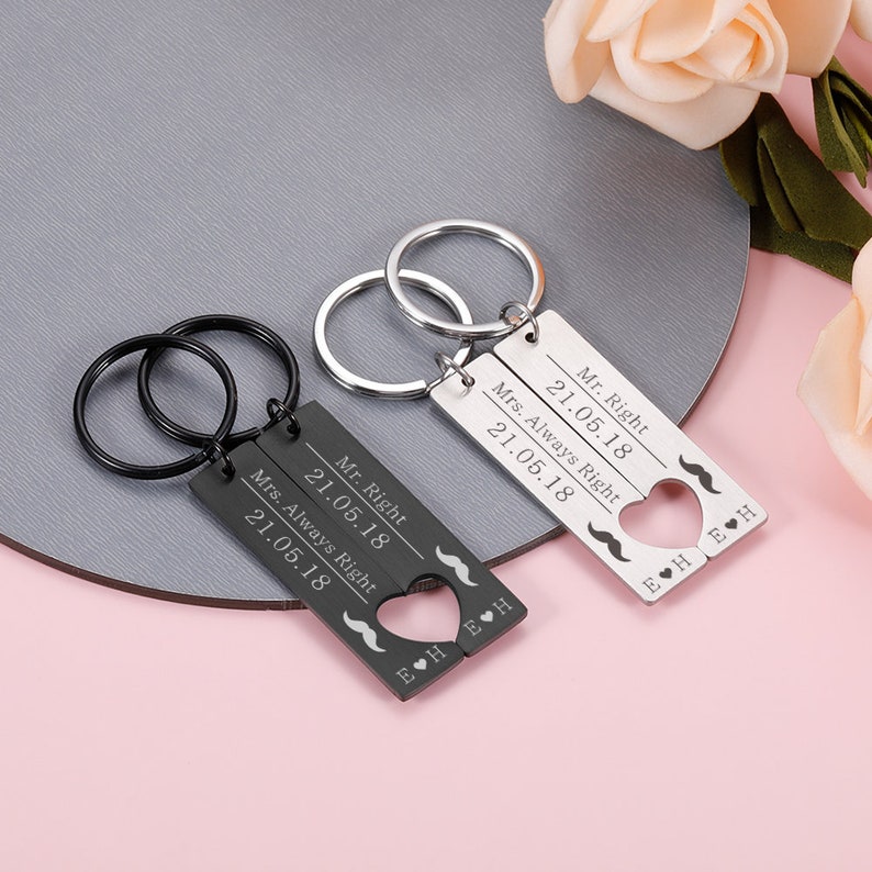 May include: A set of two black and silver keychains with engraved text that reads "Mr. Right 21.05.18" and "Mrs. Always Right 21.05.18". The keychains feature a heart shape with a mustache design.