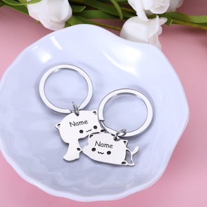 May include: Two silver keychains with cat-shaped charms. The charms have the word "Name" engraved on them.