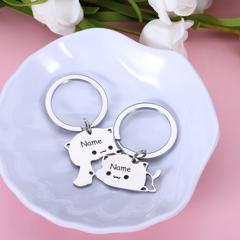 May include: Two silver keychains with cat-shaped charms. The charms have the word "Name" engraved on them.