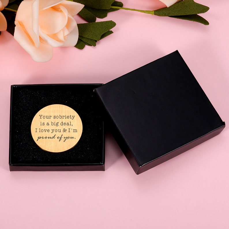 May include: A wooden circle with the text "Your sobriety is a big deal, I love you & I'm proud of you." The circle is in a black box with a black lid.