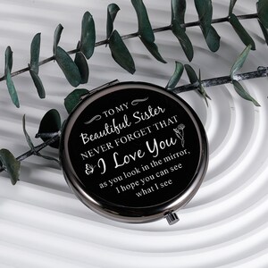 May include: A black compact mirror with a silver trim. The mirror has a message that reads "To my Beautiful Sister Never Forget That I Love You as you look in the mirror, I hope you can see what I see."