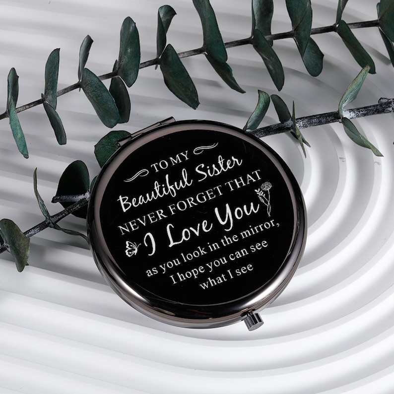 May include: A black compact mirror with a silver trim. The mirror has a message that reads "To my Beautiful Sister Never Forget That I Love You as you look in the mirror, I hope you can see what I see."