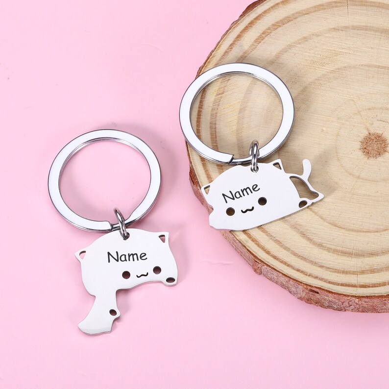 May include: Two silver keychains with cat-shaped charms. Each charm has a space for a name, and the text "Name" is engraved on each charm.