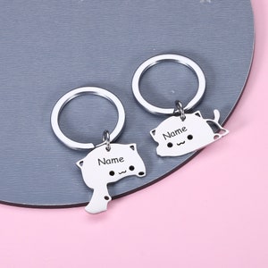 May include: Two silver keychains with cat-shaped charms. Each charm has the word "Name" engraved on it.