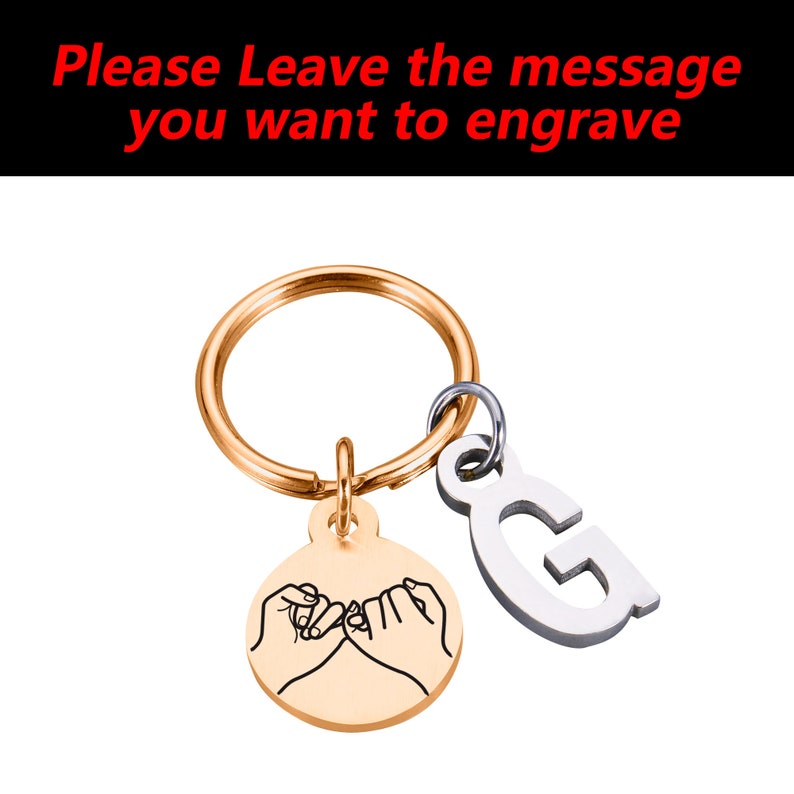 May include: Gold-tone keychain with a round charm featuring a pinky promise design and a silver charm with the letter G.