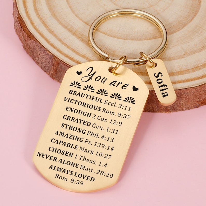 Puede incluir: Llavero dorado con una etiqueta que dice "You are" y enumera varias citas inspiradoras con vers&iacute;culos b&iacute;blicos correspondientes. Una etiqueta m&aacute;s peque&ntilde;a con el nombre "Sofia" est&aacute; unida al llavero.