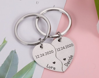 May include: Two silver keychains with split heart charms. The charms are engraved with the date "12.24.2020", the names "Lura" and "Davide", and a small heart symbol.