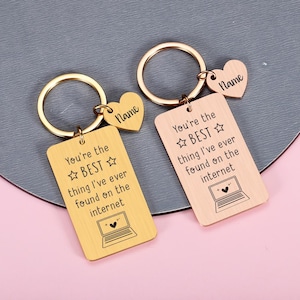 May include: Two rectangular metal keychains, one gold-toned and one rose gold-toned, each with a circular ring and a small heart-shaped charm engraved with the word Name. Both feature the text You're the BEST thing I've ever found on the internet.