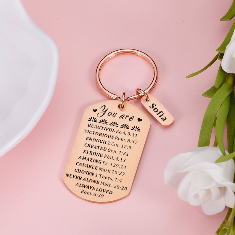 Puede incluir: Un llavero de oro rosa con un dije en forma de placa de identificaci&oacute;n que dice "You are" seguido de una lista de afirmaciones positivas y vers&iacute;culos b&iacute;blicos. La etiqueta tambi&eacute;n incluye el nombre "Sofia" en una etiqueta m&aacute;s peque&ntilde;a unida al llavero.