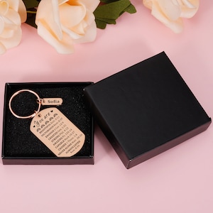 Puede incluir: Un llavero de oro rosa con una caja negra. El llavero tiene una peque&ntilde;a etiqueta con el nombre "Sofia" y una etiqueta m&aacute;s grande con el texto "You are" seguido de una lista de afirmaciones positivas y vers&iacute;culos b&iacute;blicos.