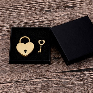 May include: A gold heart-shaped padlock and key in a black velvet box. The padlock has a keyhole and the key has a heart-shaped bow.