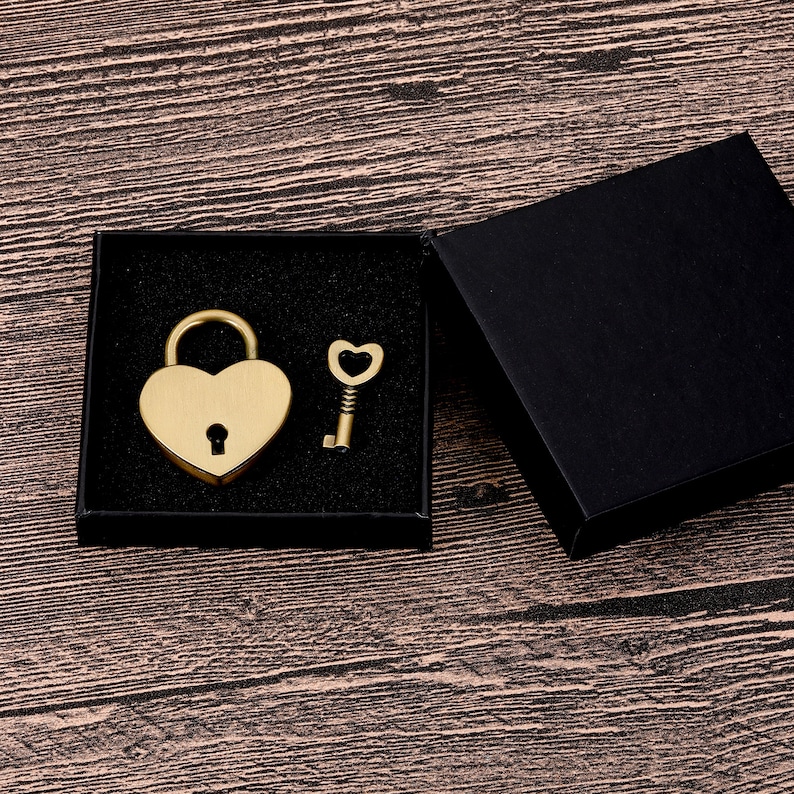 May include: A gold heart-shaped padlock and key in a black velvet box. The padlock has a keyhole and the key has a heart-shaped bow.