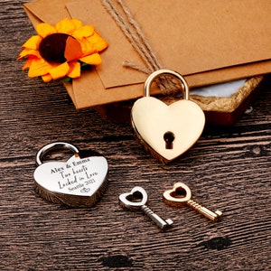 May include: Two heart-shaped padlocks and two keys. One padlock is silver and engraved with the text "Alex & Emma Two hearts Locked in Love Seattle 2021". The other padlock is gold.