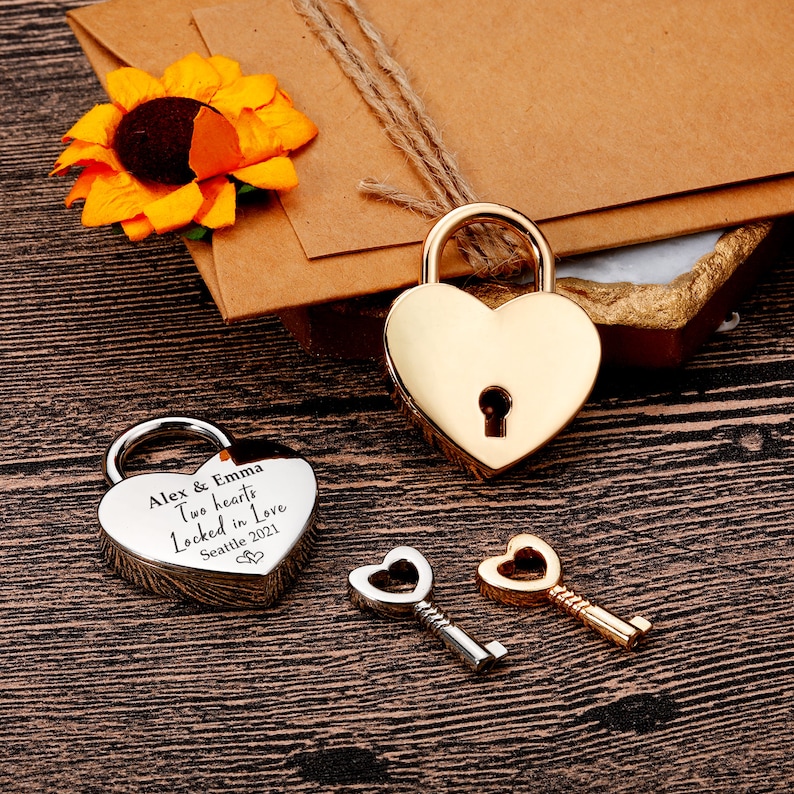 May include: Two heart-shaped padlocks and two keys. One padlock is silver and engraved with the text "Alex & Emma Two hearts Locked in Love Seattle 2021". The other padlock is gold.