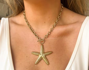 May include: A gold chain necklace with a large gold starfish pendant. The chain is a thick, chunky style.