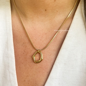 May include: A gold chain necklace with a gold pendant shaped like an irregular circle. The necklace is worn by a person with a white shirt.