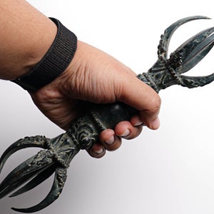 May include: A hand holds a black metal ritual weapon with a curved, ornate handle and three sharp points.