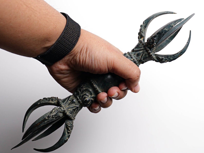 May include: A hand holds a black metal ritual weapon with a curved, ornate handle and three sharp points.